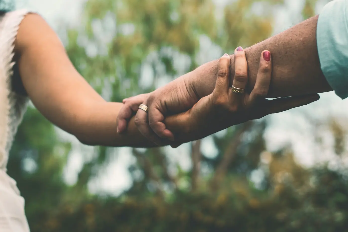 Two hands holding on to each other, trees behind them