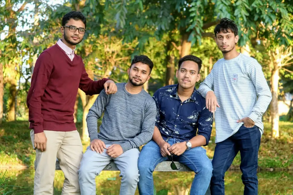 Four friends sitting together on a park bench, smiling at the camera